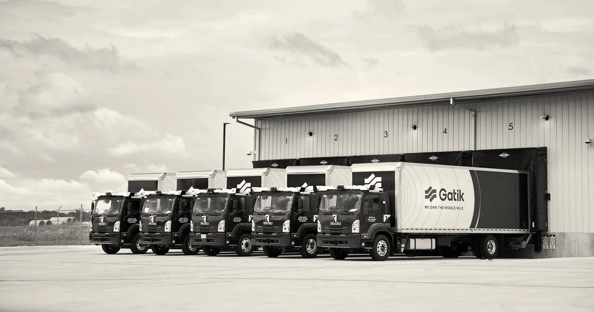 A fleet of purple and white Gatik autonomous delivery trucks parked at warehouse loading bays