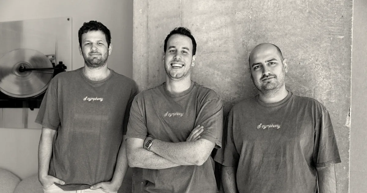 Three co-founders of Cymphony smiling together wearing matching purple t-shirts with company branding.