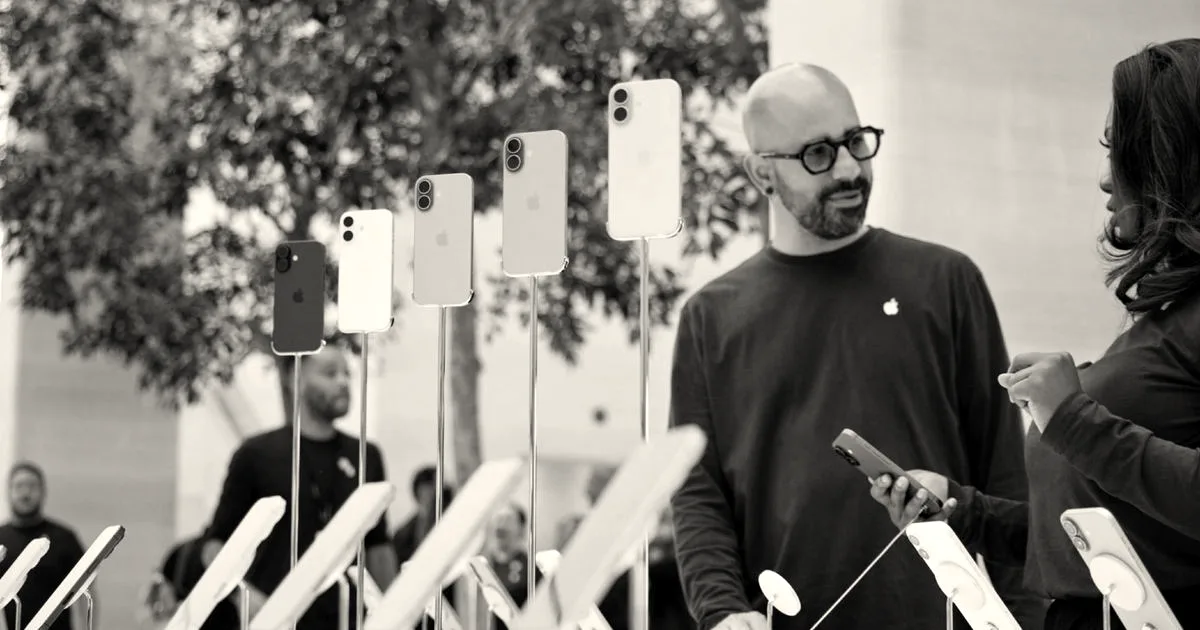 An Apple Store employee displaying various iPhone models on stands to a customer inside the store.