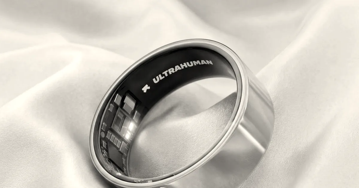 A gold Ultrahuman smart ring resting on light silk fabric displaying visible internal sensors and branding.
