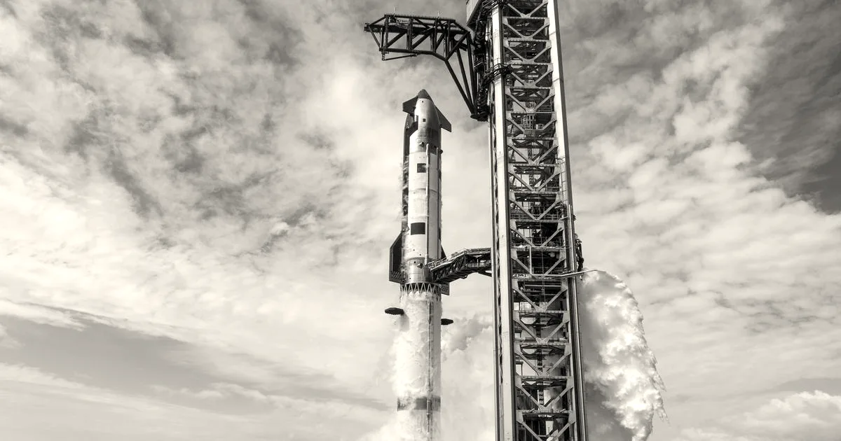 SpaceX Starship rocket on the launch pad surrounded by white steam under a blue sky with clouds.