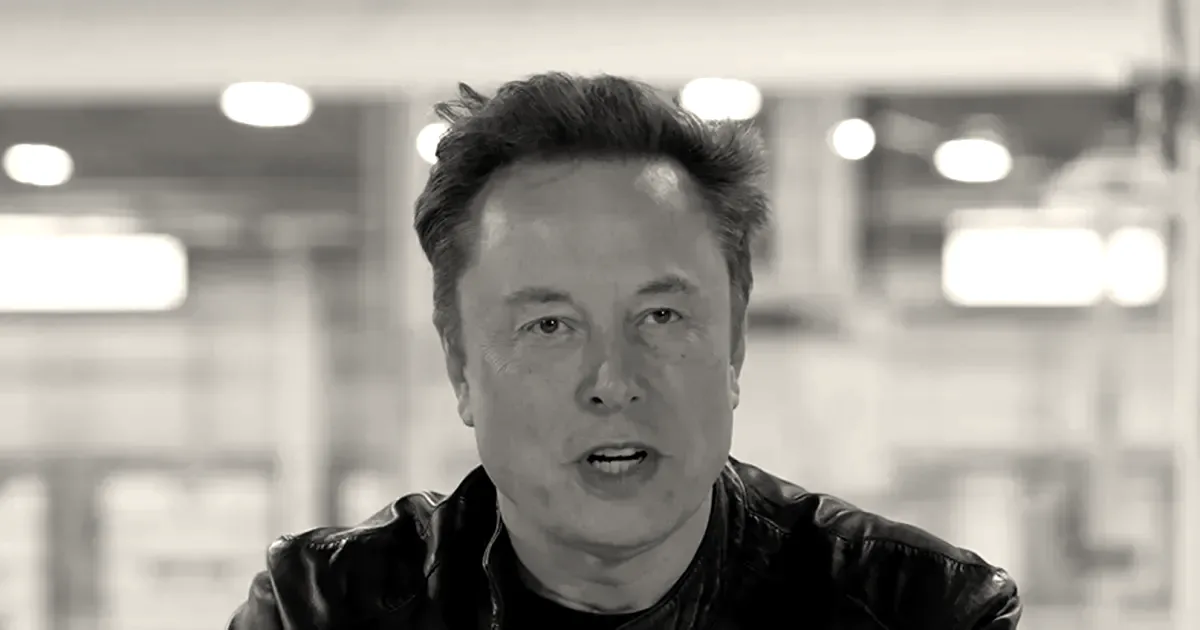 Elon Musk wearing a black leather jacket during an interview in an industrial setting.
