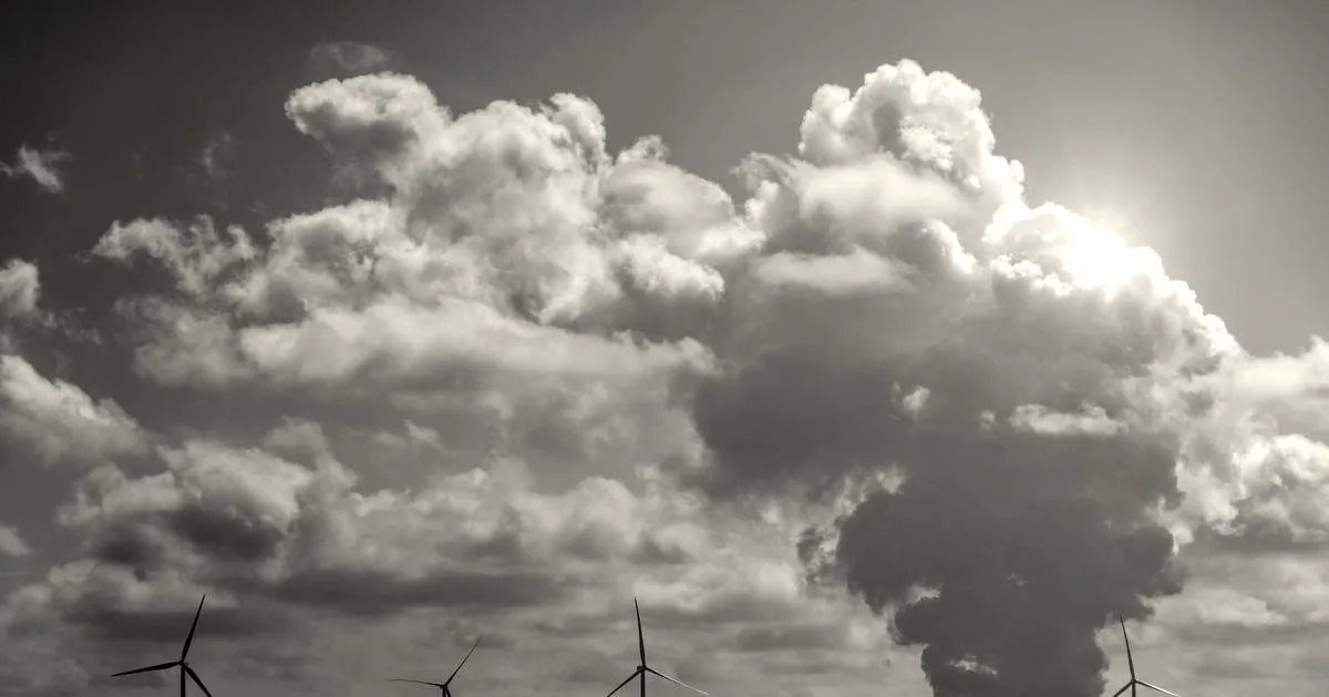 Wind turbines and a power plant under dramatic cumulus clouds in a rural landscape.