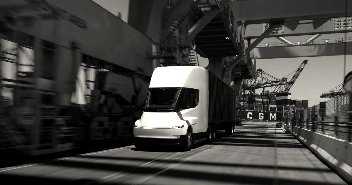 A white Tesla Semi truck hauling a cargo trailer driving along an industrial port road.