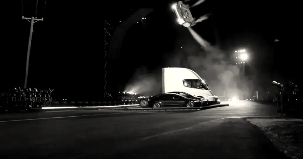 A white sports car suspended mid-air in front of a semi truck at a nighttime demonstration.