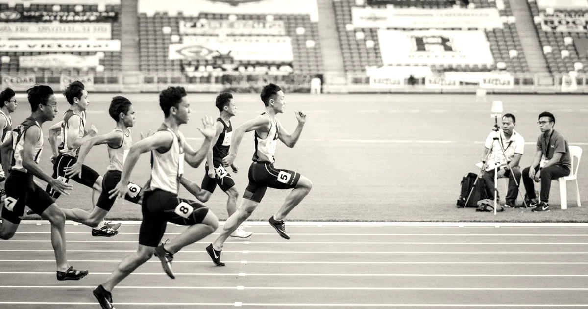 Group of sprinters exploding out of the starting blocks in a track race at a stadium.