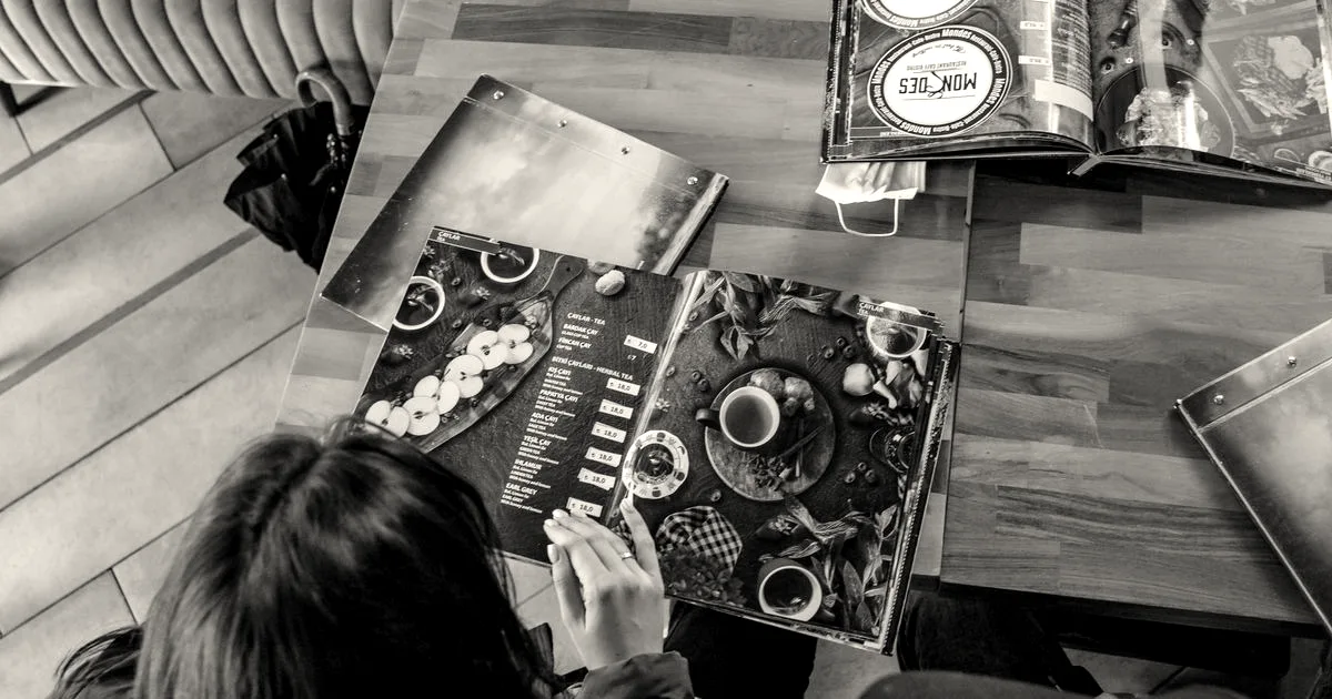 Top-down view of people sitting at a wooden café table browsing colorful illustrated restaurant menus.