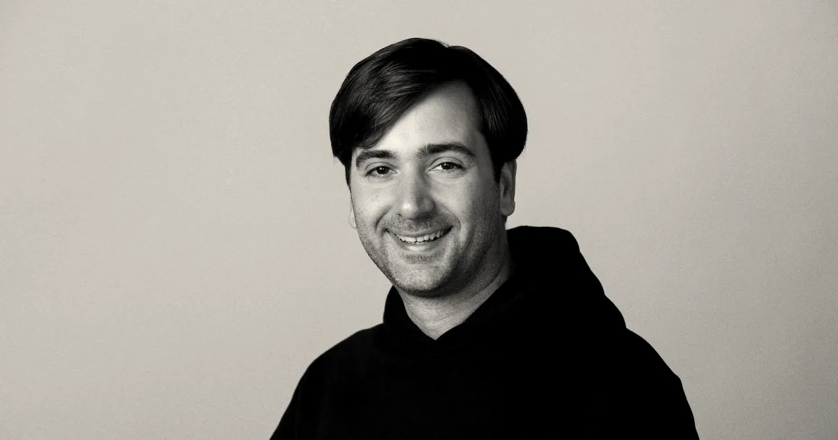 Close-up portrait of Thibault Sottiaux smiling in a black hoodie against a plain gray background.
