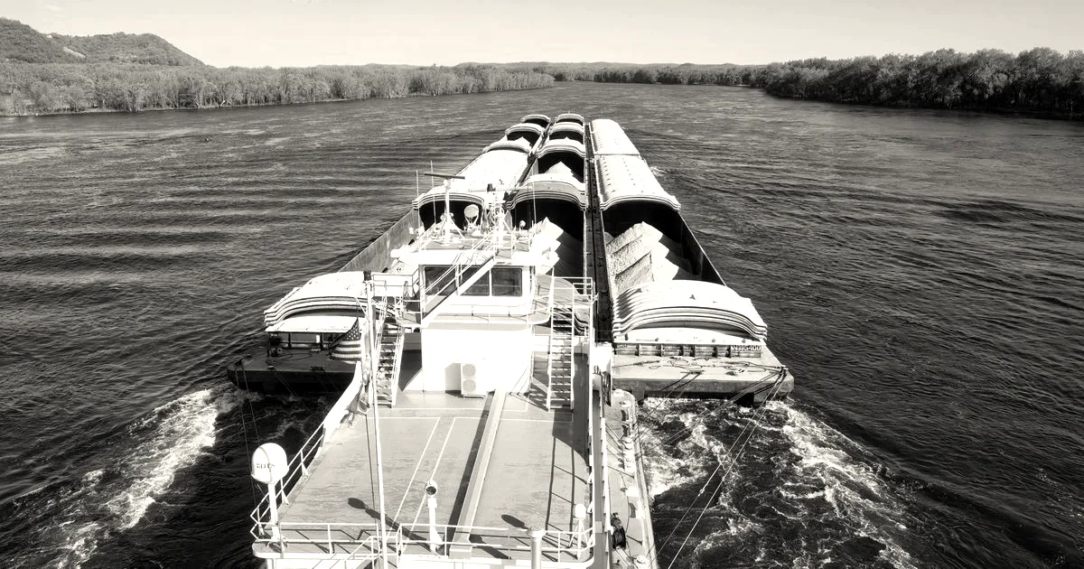 An aerial view of a large cargo barge navigating the Mississippi River under clear skies.