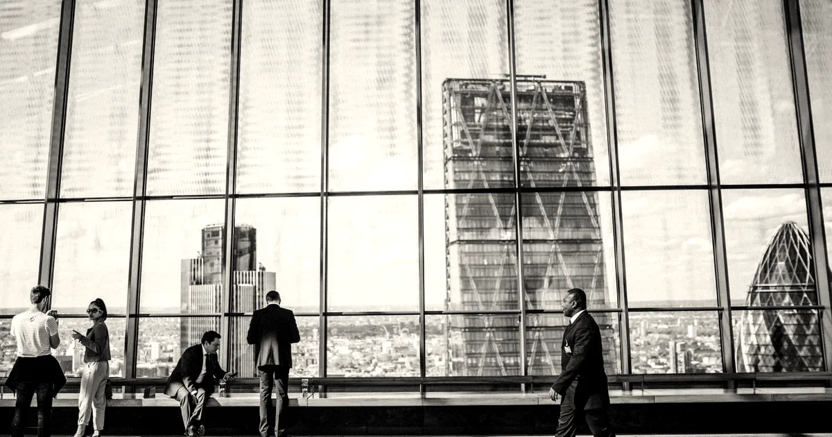 Business professionals standing and walking in a modern high-rise office with large windows overlooking city skyscrapers.
