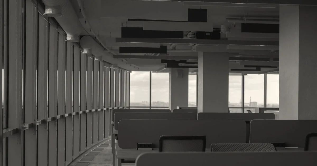 An empty modern office interior with rows of gray cubicles beside large glass windows.
