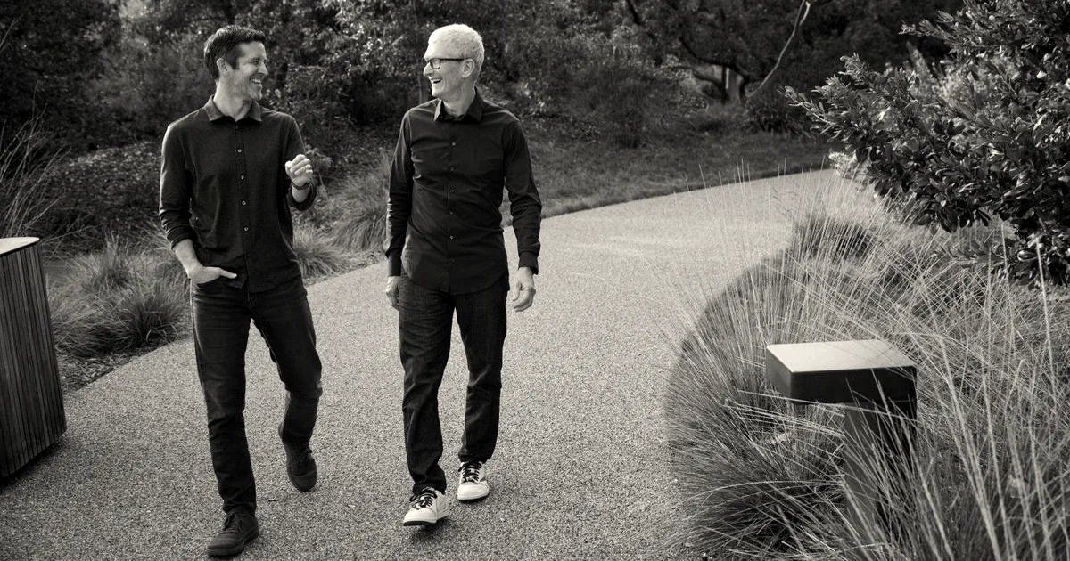 Apple CEO Tim Cook and hardware engineering executive John Ternus walking along an outdoor path together.
