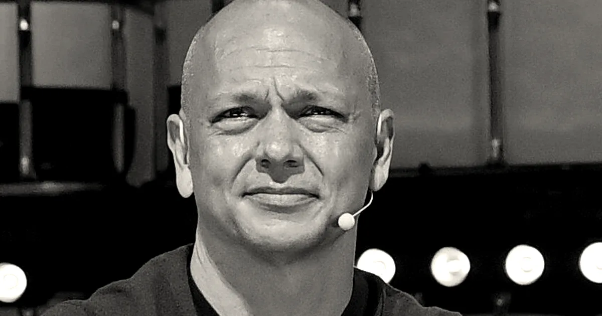 Tony Fadell wearing an olive green sweater clapping his hands on stage at an event