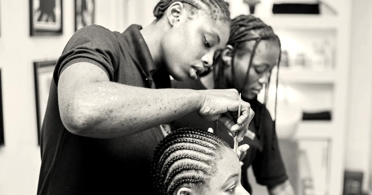 A hairstylist meticulously braiding cornrows into a woman's hair in a salon setting