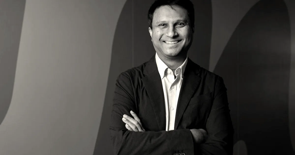 Portrait of Truecaller CEO Rishit Jhunjhunwala smiling with arms crossed against a blue background.
