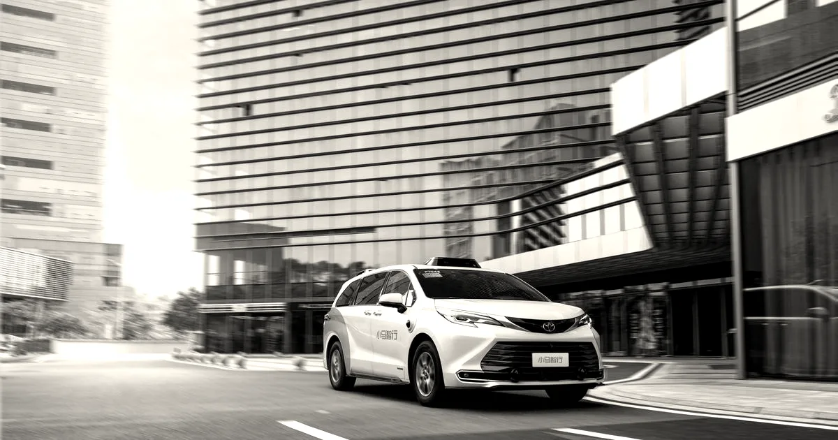 A white Pony.ai autonomous robotaxi minivan driving along a modern city street in front of glass buildings