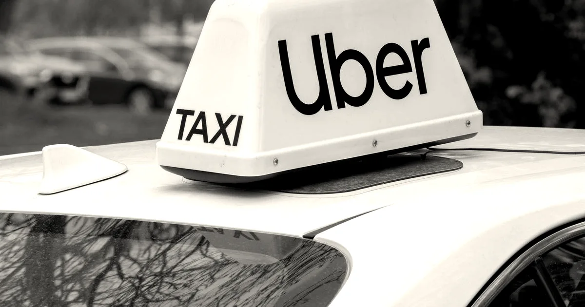 A white illuminated Uber taxi sign mounted on the roof of a car outdoors.