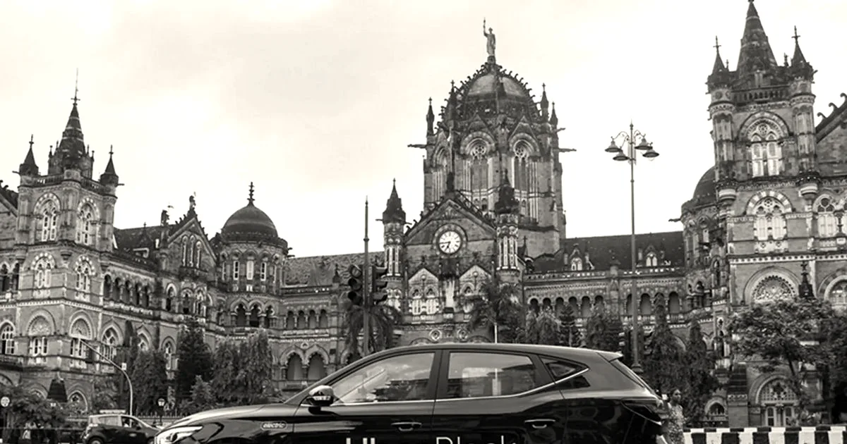 A black Uber car parked in front of Mumbai's historic Chhatrapati Shivaji Maharaj Terminus railway station.