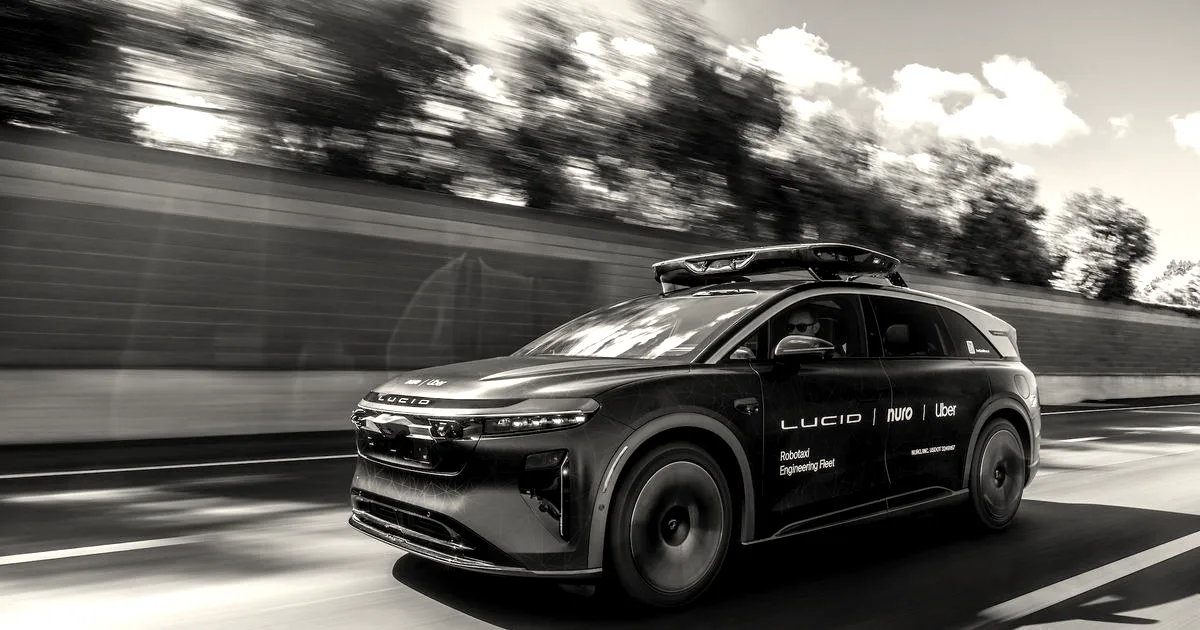 A dark grey Lucid vehicle with autonomous driving sensors on top drives on a highway, branded with Lucid, Nuro, and Uber logos.