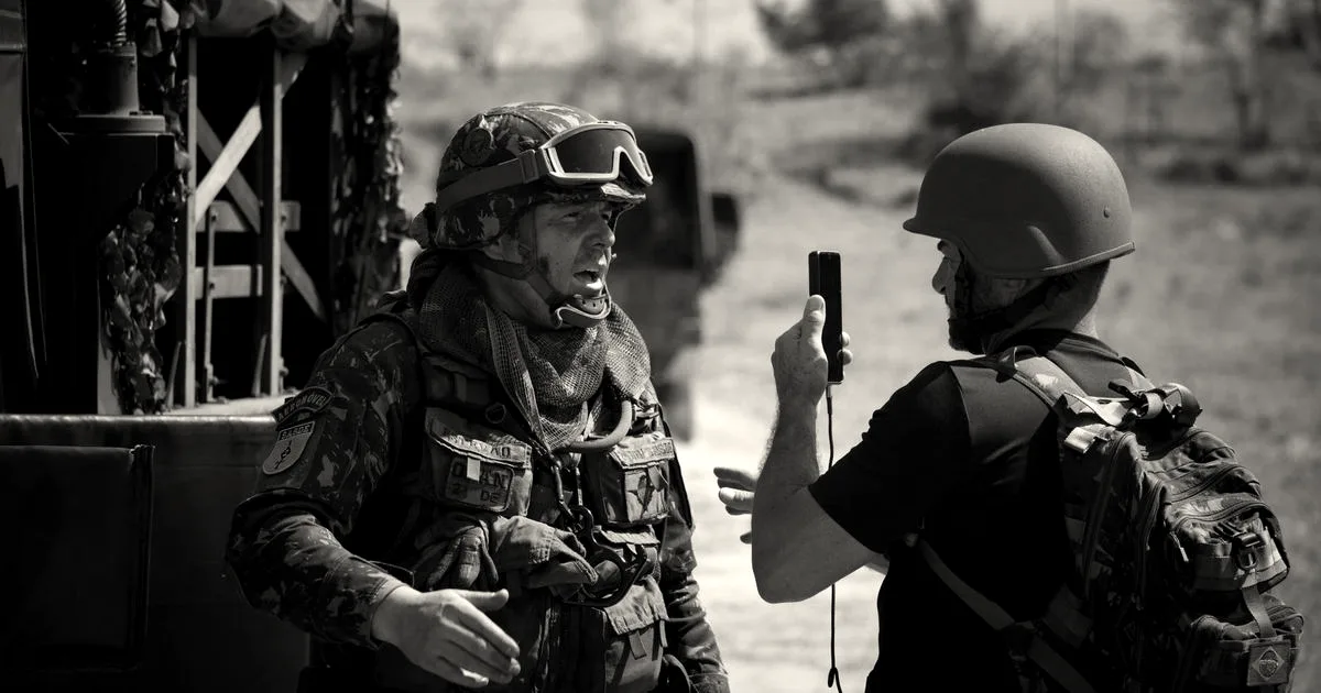 Two soldiers in full gear having a tactical discussion outdoors beside military vehicles.