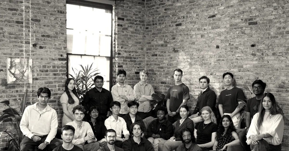 A diverse group of team members sitting and standing together against an exposed brick wall.