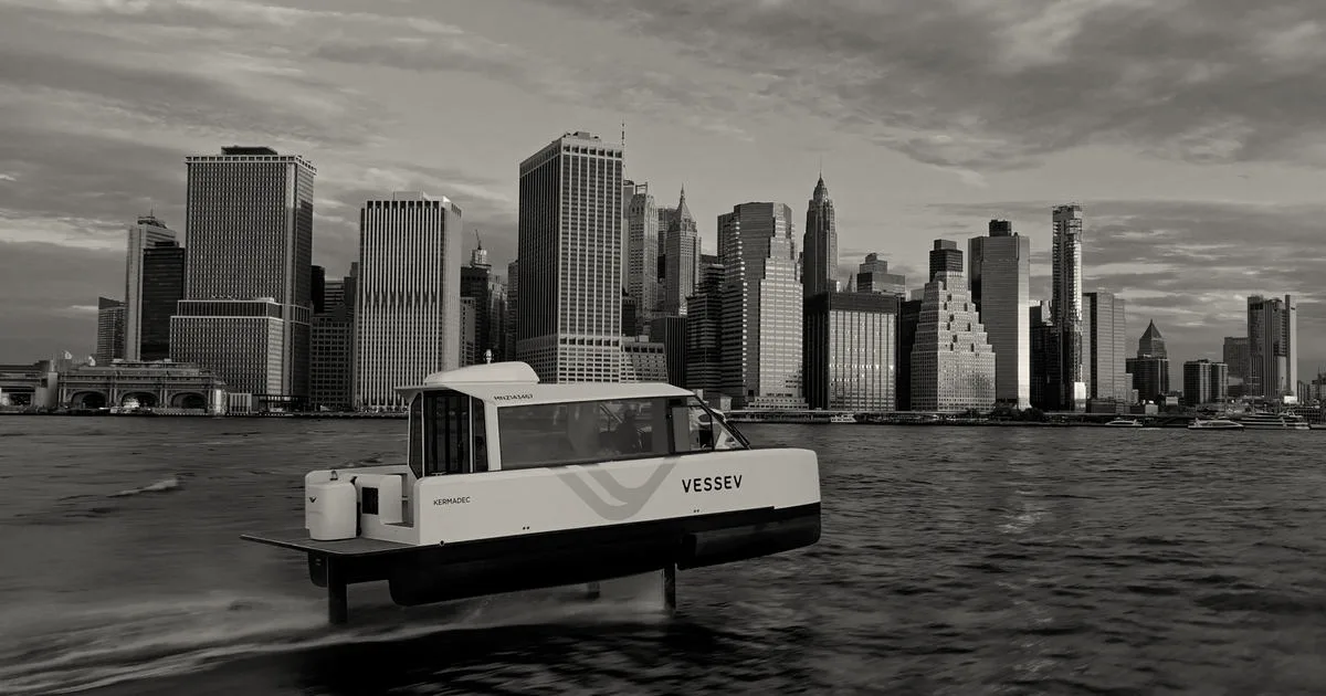 An electric hydrofoil ferry by Vessev cruising above the water against the Lower Manhattan skyline.