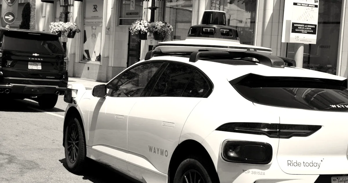 A white Waymo autonomous vehicle fitted with roof-mounted sensors parked along a city street.