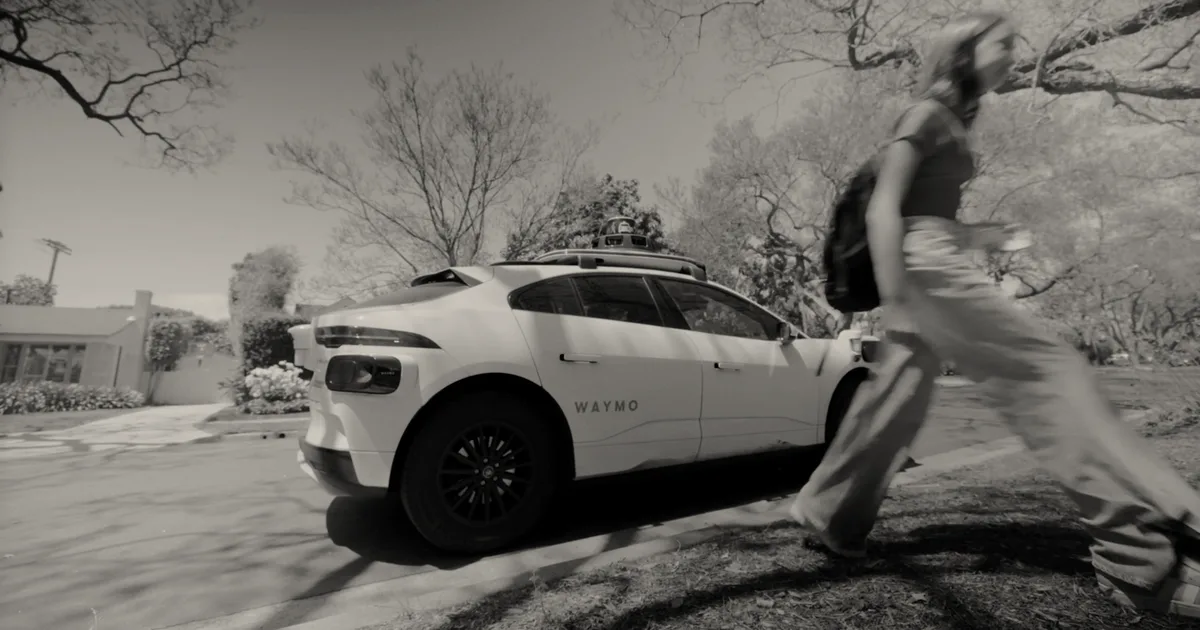 A white Waymo self-driving vehicle parked on a residential street as a teenage girl walks by.