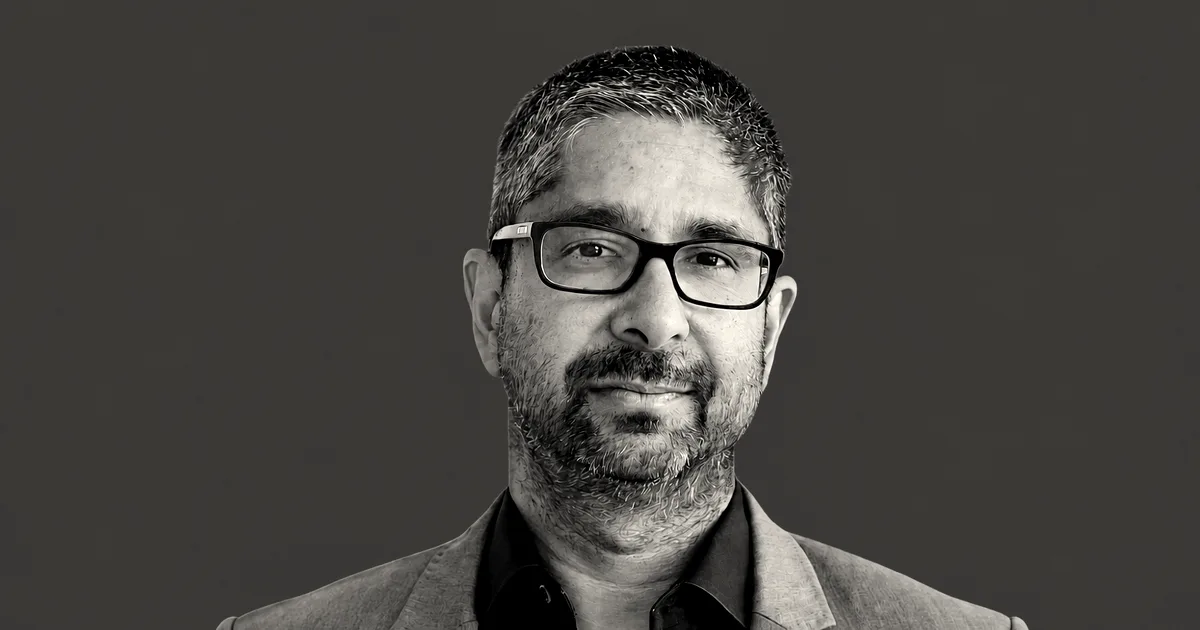Portrait of Vijay Pande wearing glasses and a grey jacket against a solid red background.