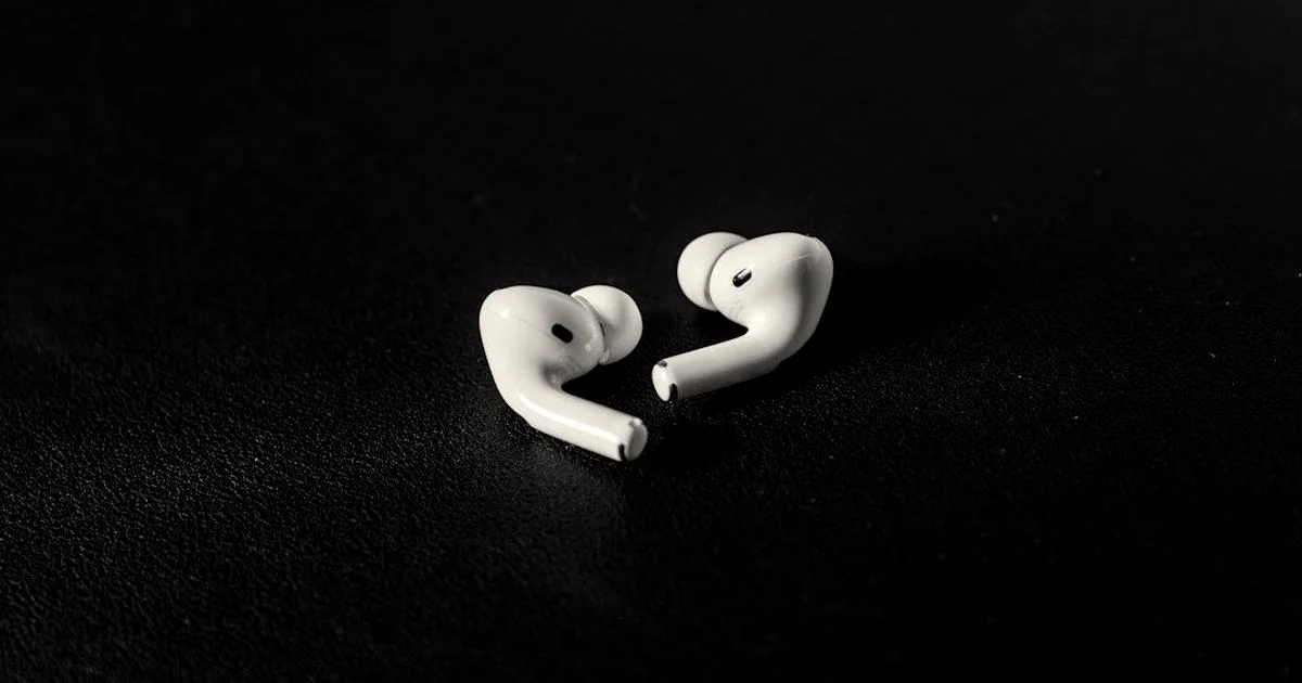 A pair of white Apple AirPods Pro earphones resting on a dark surface.