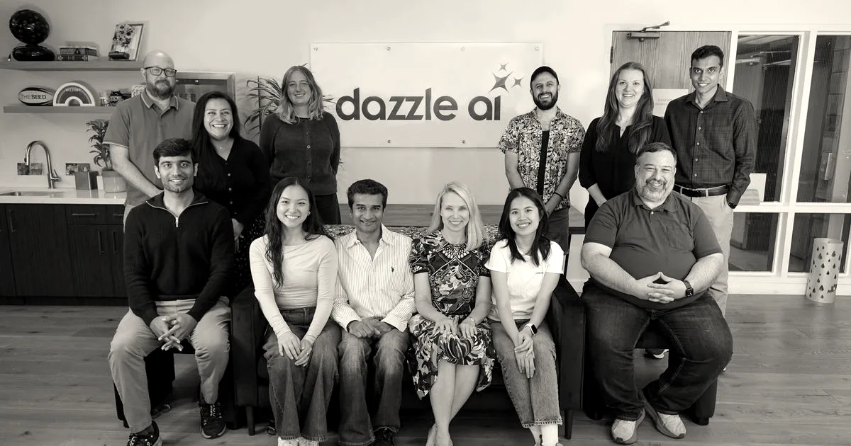 Marissa Mayer and the Dazzle AI team sitting and standing together in front of a company logo sign.