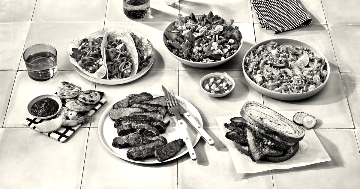 An assortment of prepared dishes including tacos, steak, salad, and a sandwich arranged on green tiles.