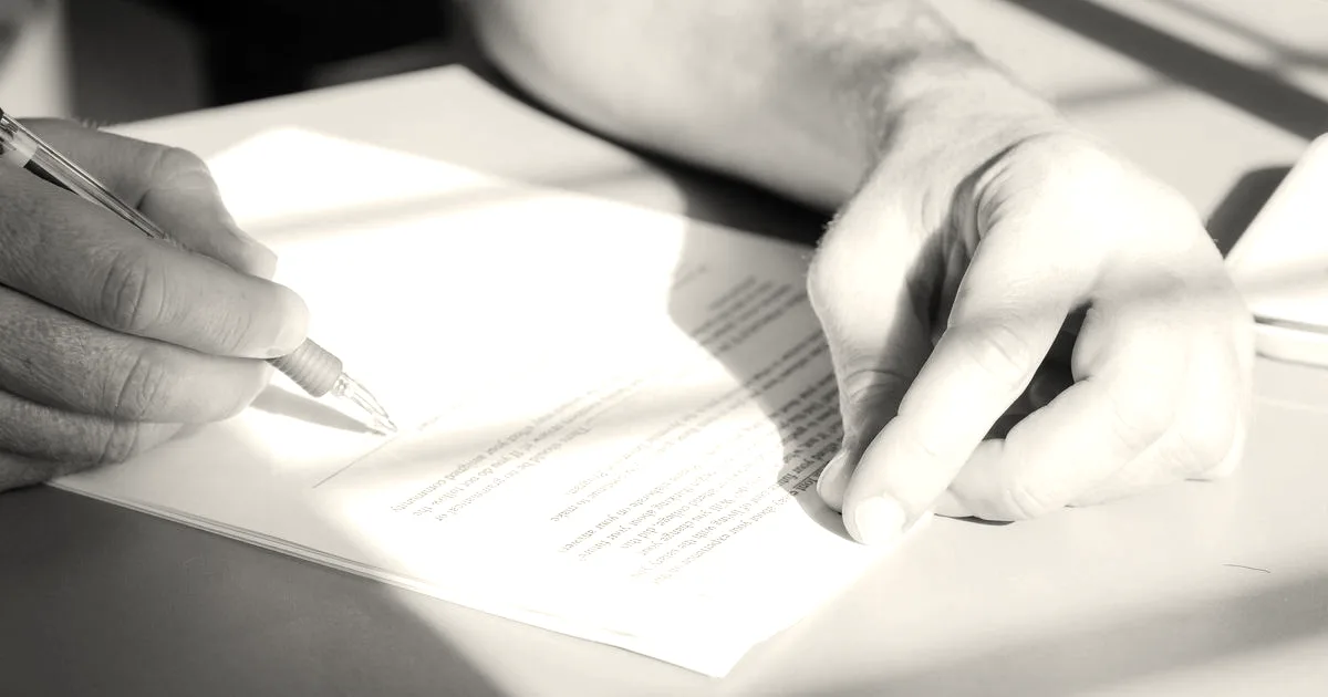 Close-up of a person's hands holding a pen and preparing to sign a paper legal document