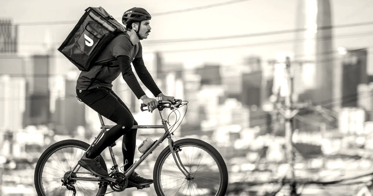 A DoorDash delivery person riding a bicycle through San Francisco with a red thermal delivery backpack.