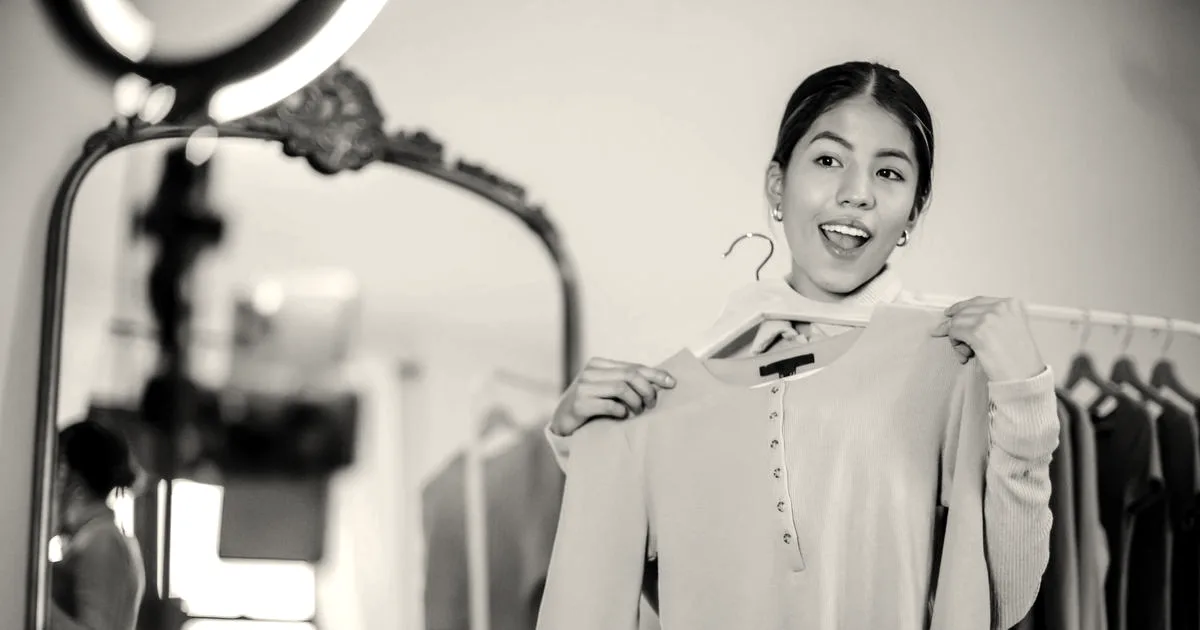 A content creator showing a green blouse on a hanger while filming a video in front of a mirror setup.