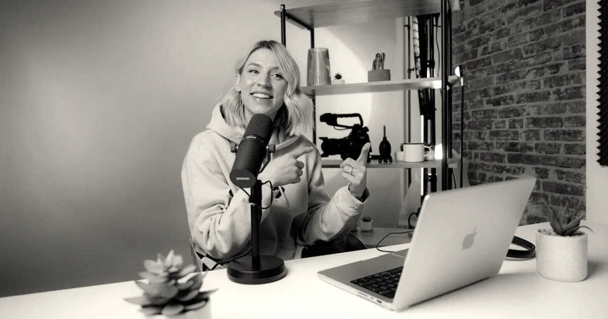 A woman sitting at a desk with a microphone and laptop in a colorful video studio setup