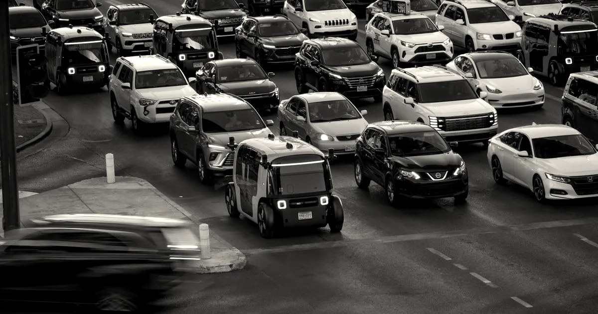 A Zoox autonomous robotaxi driving through traffic surrounded by conventional cars at a busy intersection.